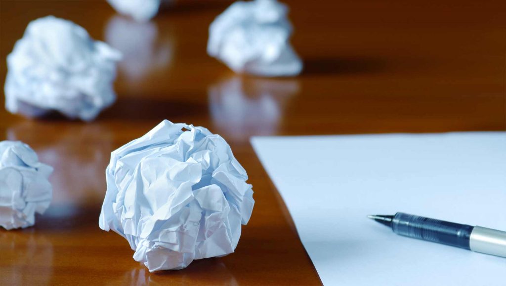 crumpled up pieces of paper on a desk next to a piece of paper and pen