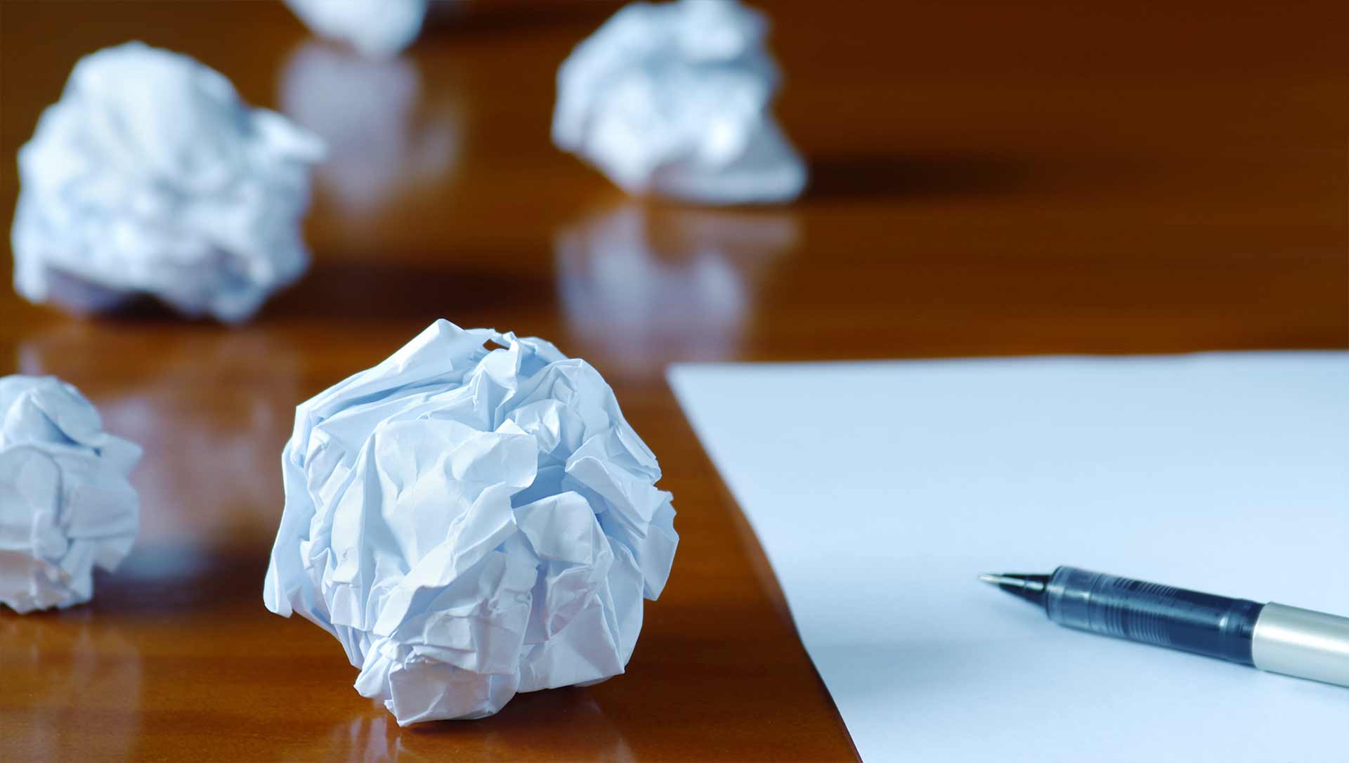 crumpled up pieces of paper on a desk next to a piece of paper and pen