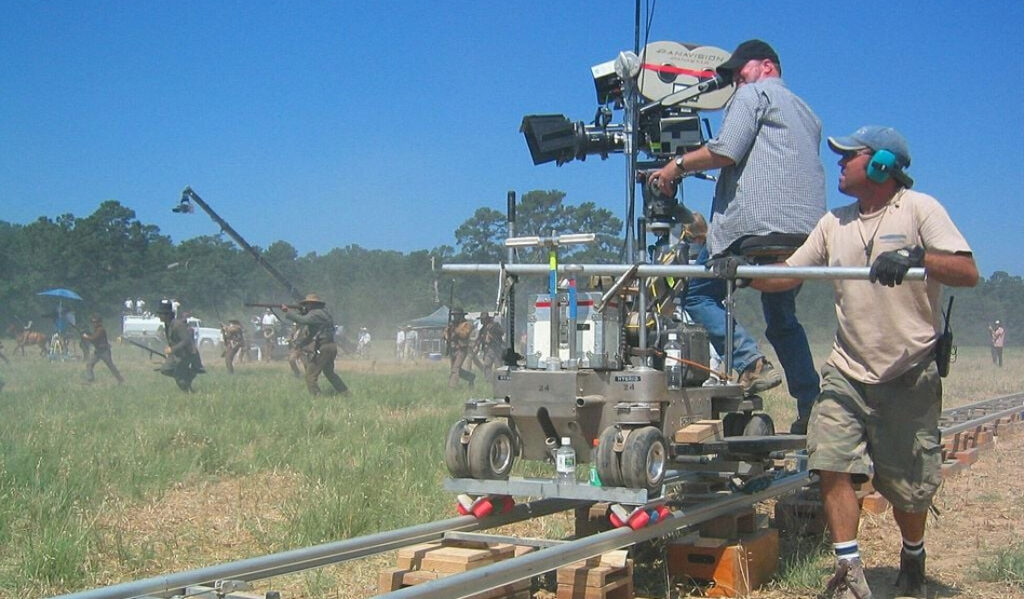 Camera operator being pushed along tracks on dolly to illustrate cinematographer equipment