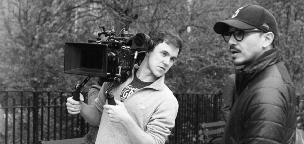 Someone holding a camera while another looks on (BW) to illustrate how much do cinematographers make.